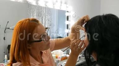 红发造型师化妆师在美容院做时尚的黑色长发模特晚妆